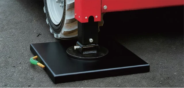 Equipment outrigger foot resting on a black rectangular support pad on pavement